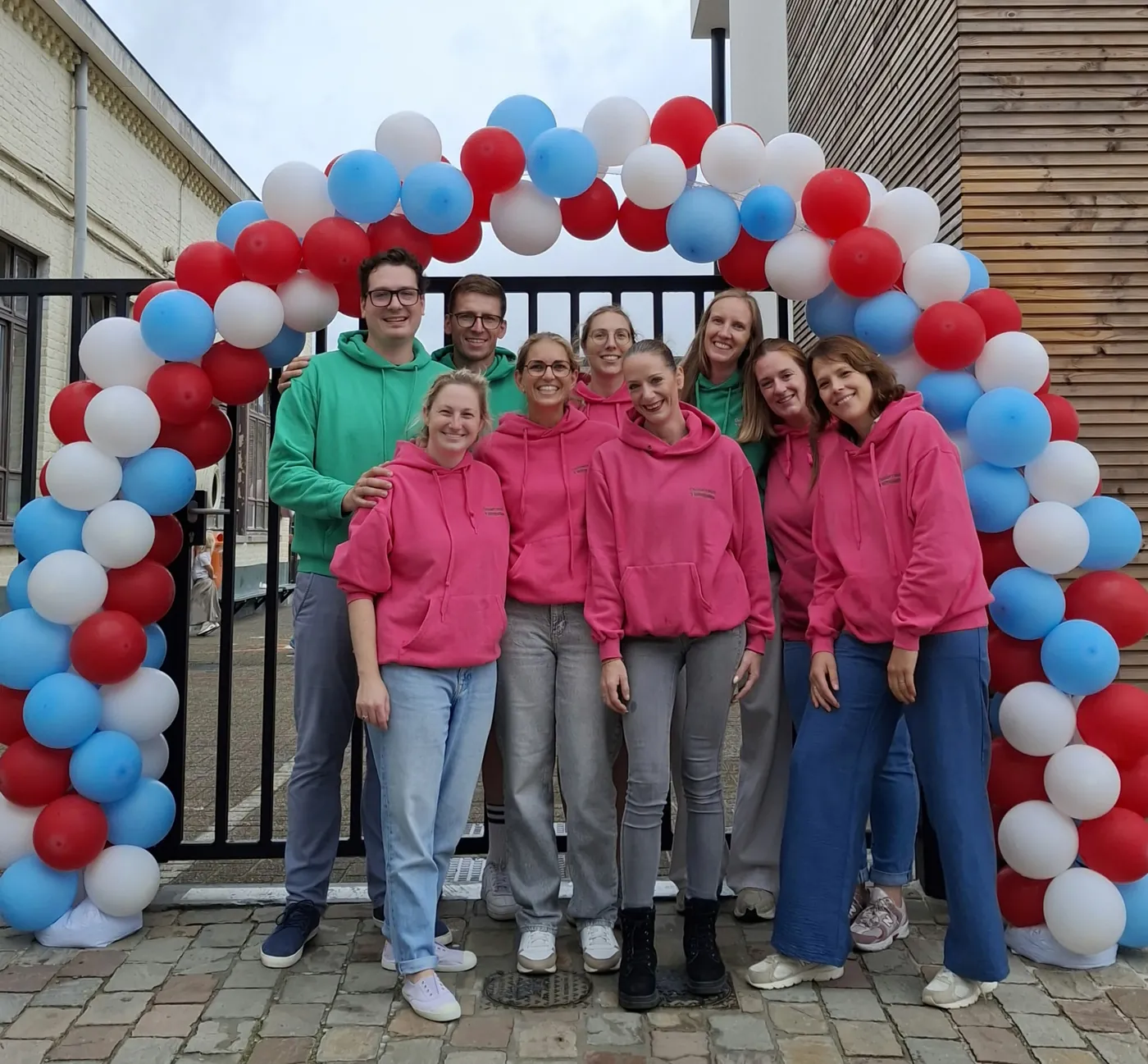 De leden van de ouderraad, lachend onder een ballonnenboog aan de schoolpoort